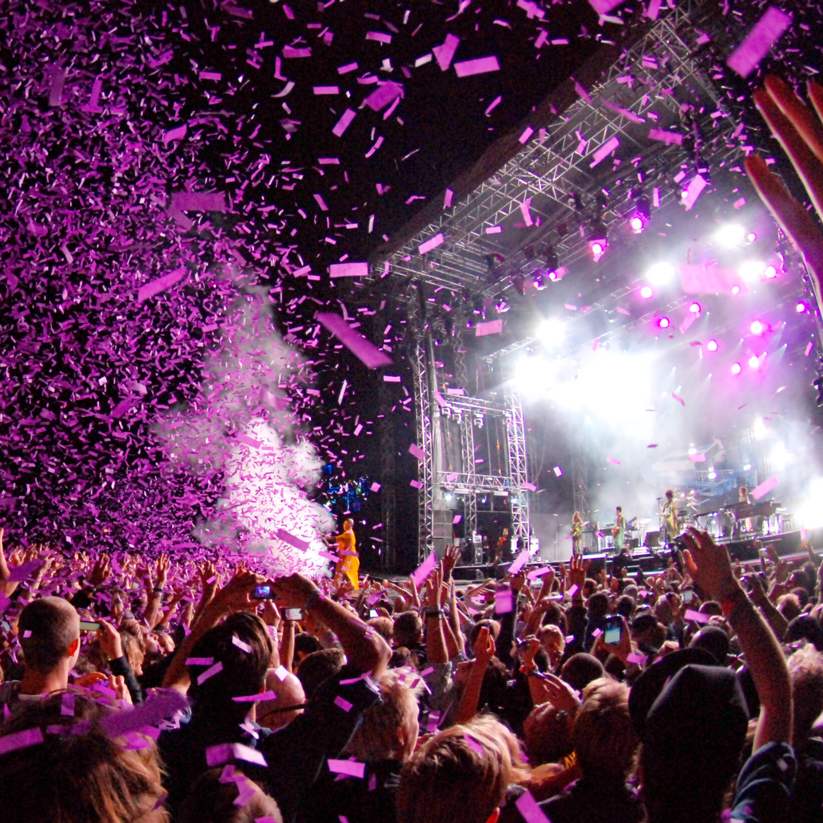 Big audience at a concert, with purple confetti flying in the air.