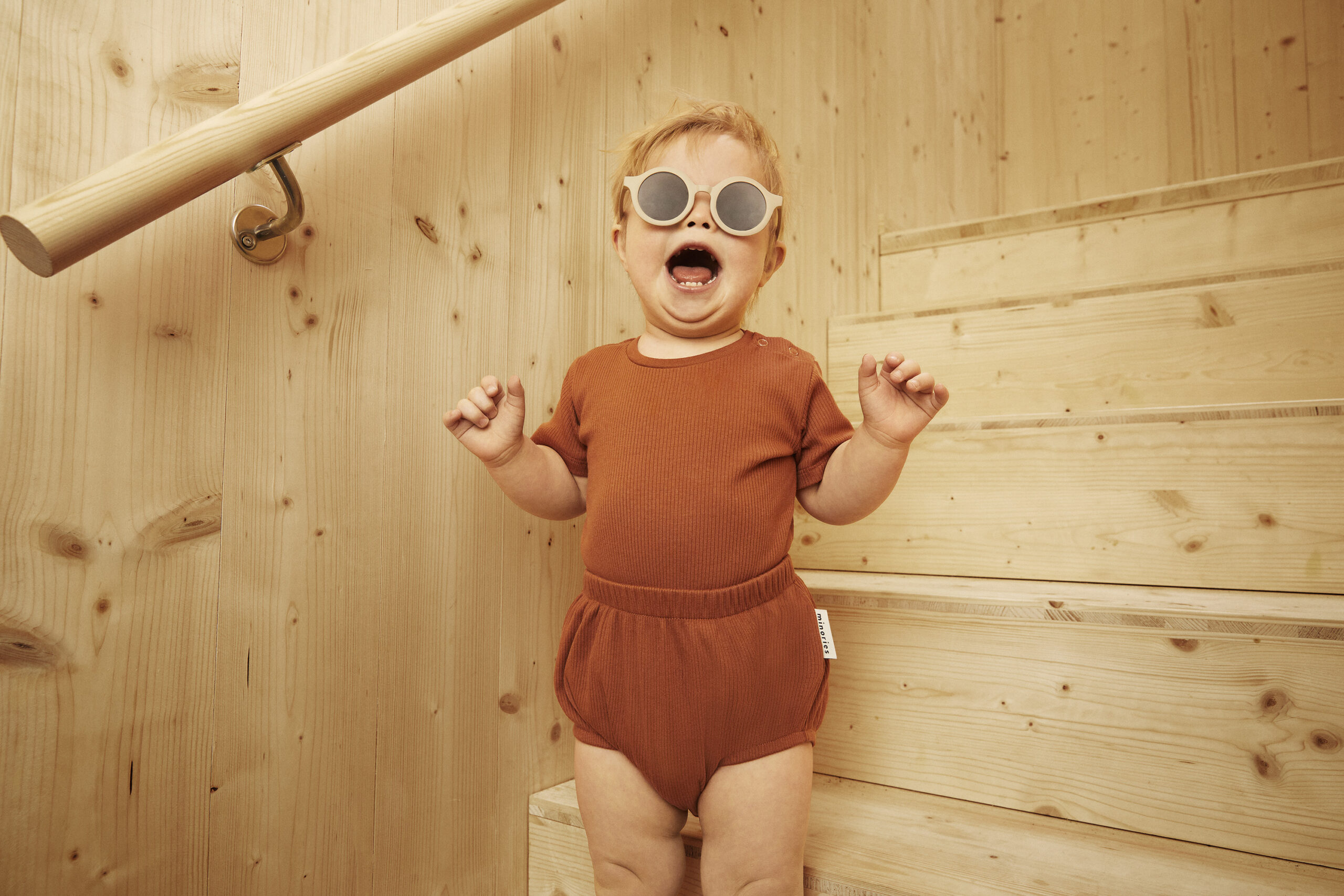 A happy toddler wearing sunglasses and sustainable clothing.